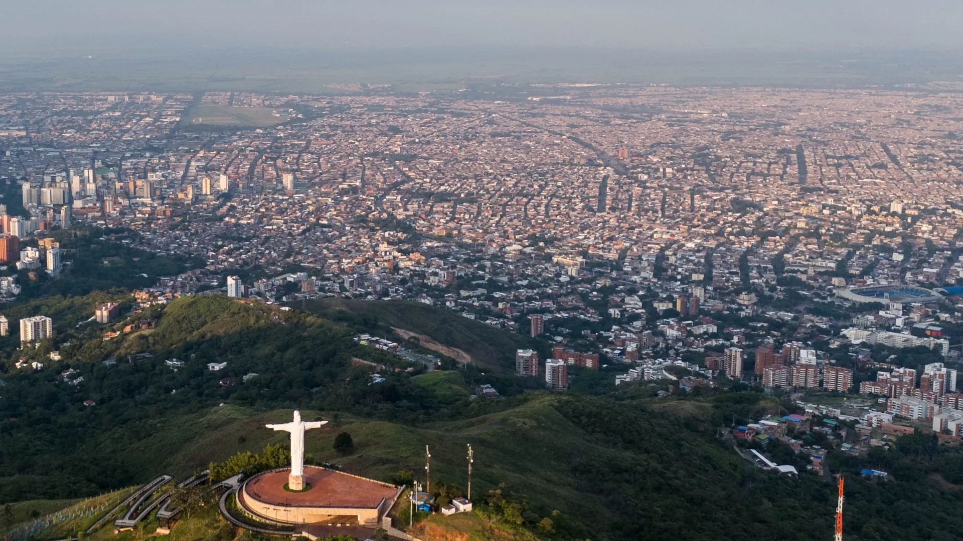 Vista aérea de Cali al amanecer, con el Cristo Rey sobre el cerro de Los Cristales y la ciudad extendida al fondo